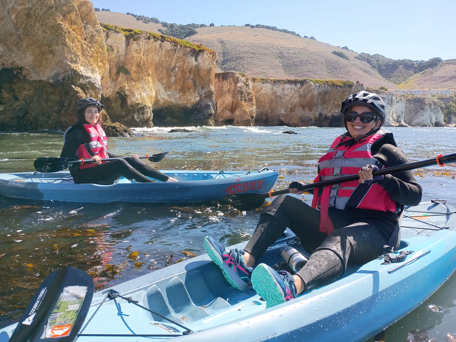Smiling guests paddling beneath the Central Coast cliffs