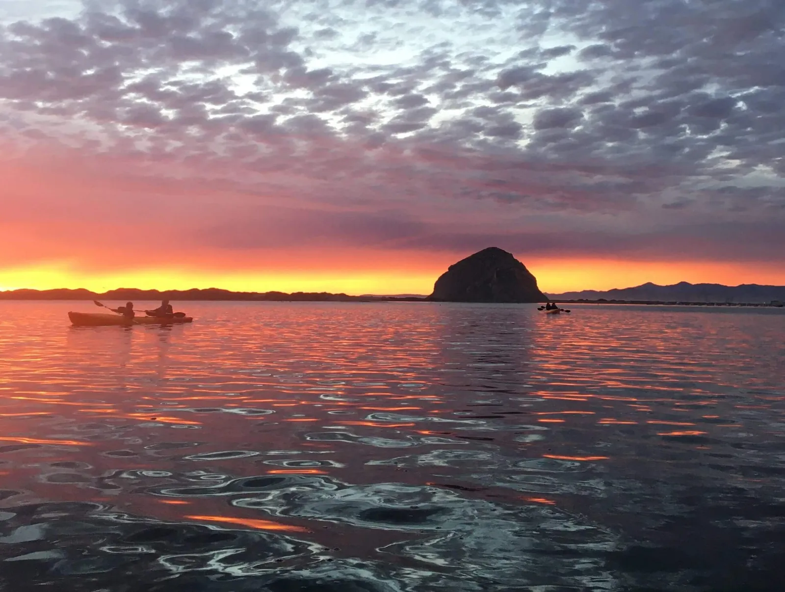 Kayakers paddling past Morro Rock at sunset